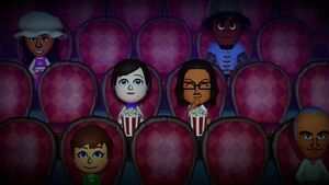Two Miis sitting in the audience chairs of a movie theater in the dark. There are some Miis sitting in chairs near them.